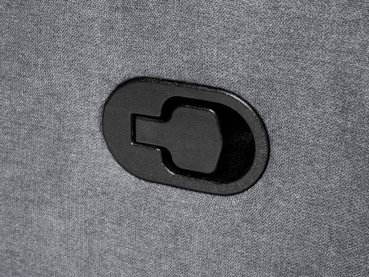 A close-up of a black oval-shaped plastic component with a keyhole-shaped cutout, mounted on a textured gray fabric surface.