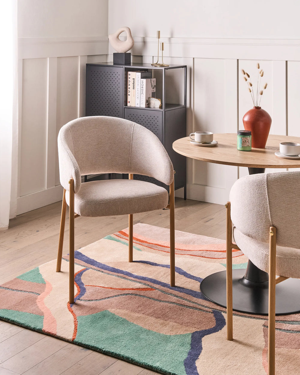Modern dining room with beige chairs, a round table, and a colorful rug.