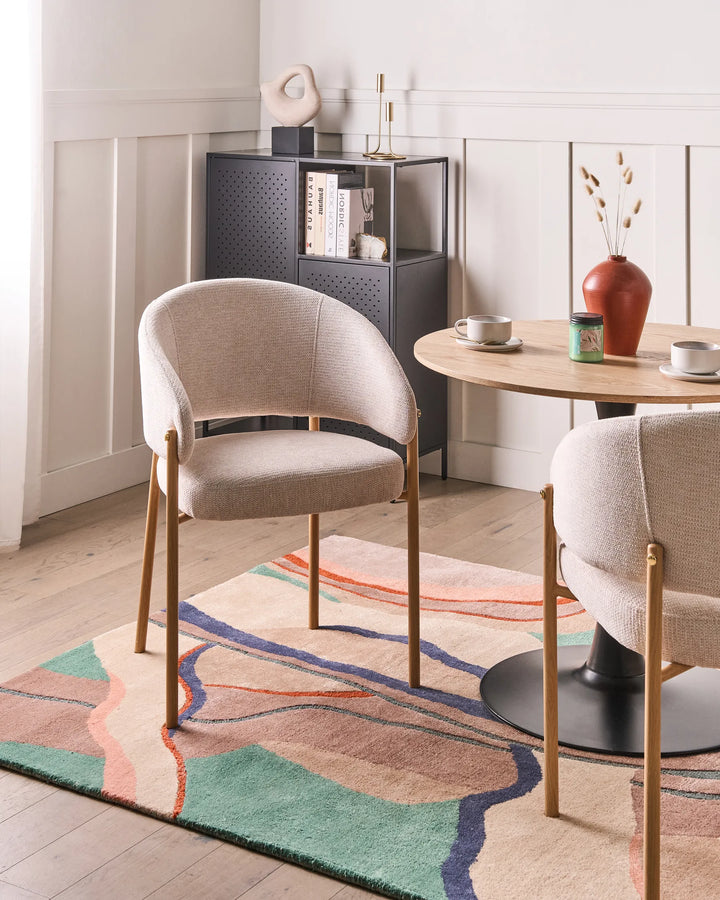 Modern dining room with beige chairs, a round table, and a colorful rug.