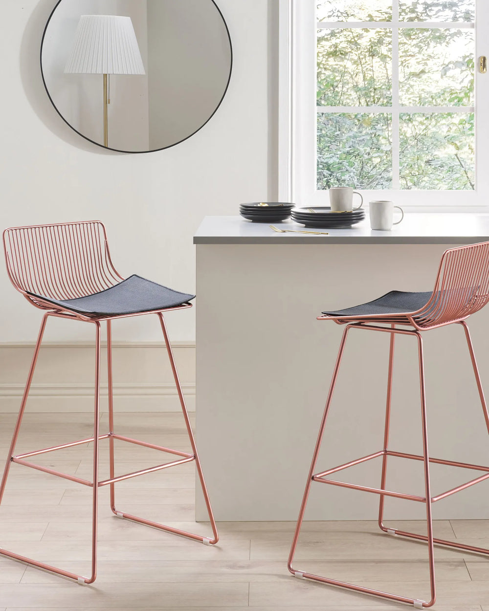 A modern wire bar stool with a copper-toned metal frame and a black seat cushion.