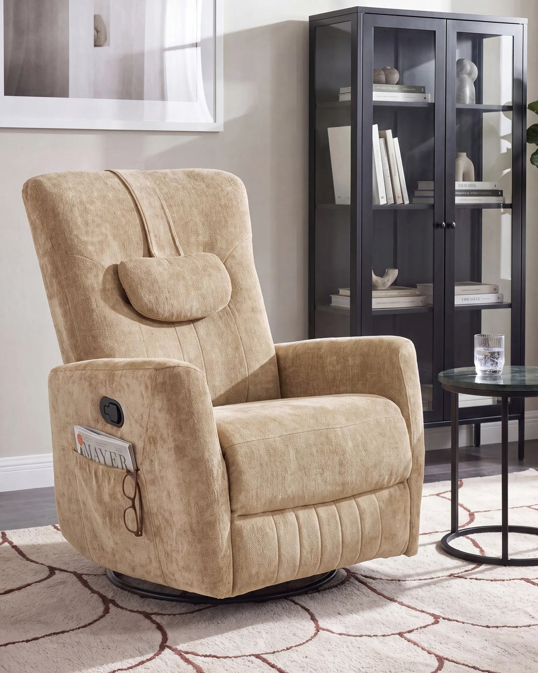 A beige upholstered recliner chair with a matching headrest pillow, shown in a styled living room setting with a dark glass display cabinet, a small round side table, and a patterned rug.