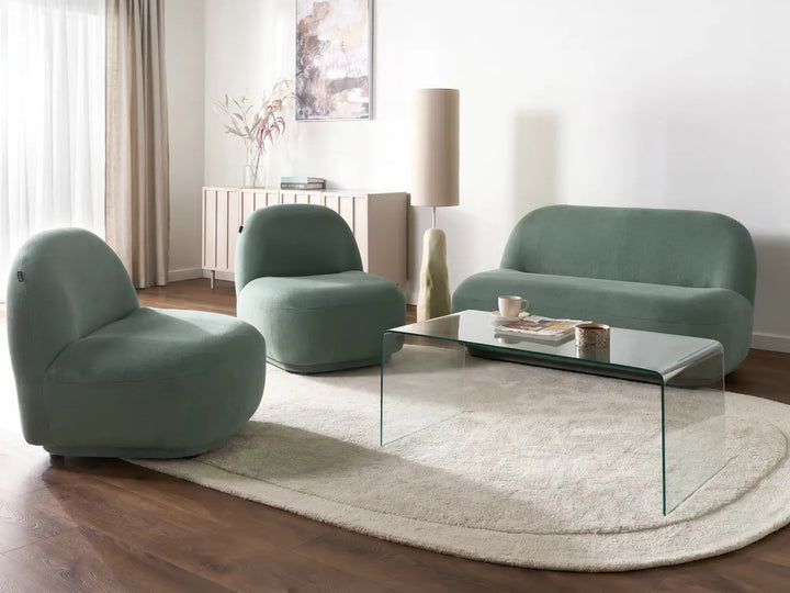 Modern living room with green chairs and a glass coffee table on a wooden floor.