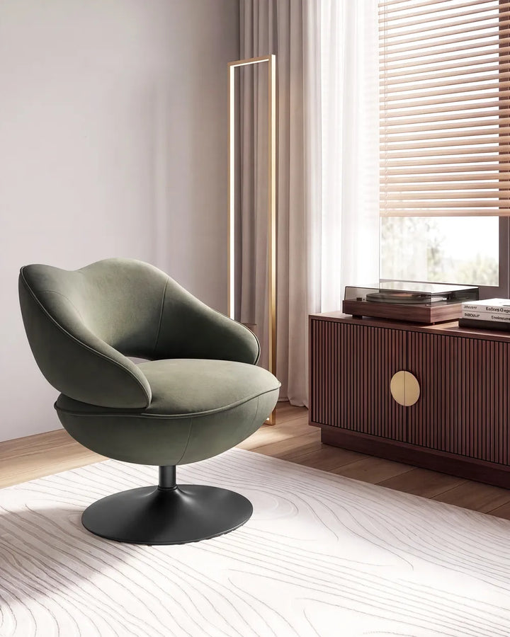 A modern swivel lounge chair upholstered in textured sage green fabric with a black circular pedestal base, set in a minimalist room next to a wooden cabinet and window.
