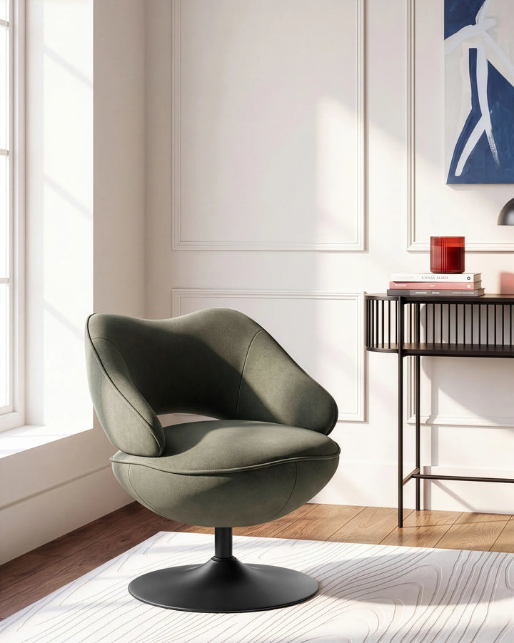 A modern swivel lounge chair in a muted sage green fabric with a black pedestal base, positioned in a bright, contemporary room with white walls, a window, and a side table.