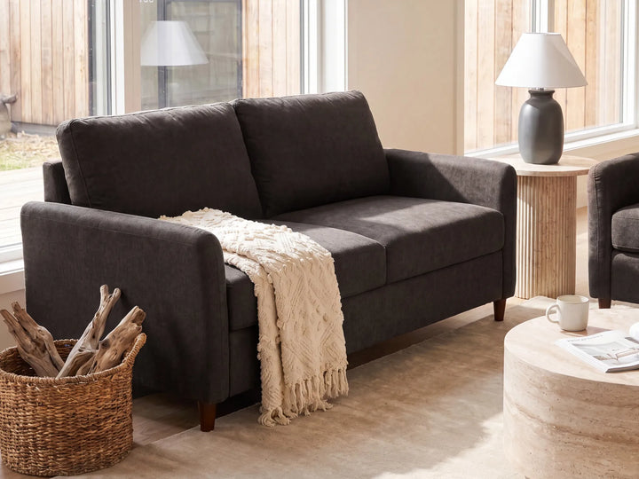 A dark brown upholstered loveseat in a bright living room setting, styled with a cream throw blanket draped over the seat.