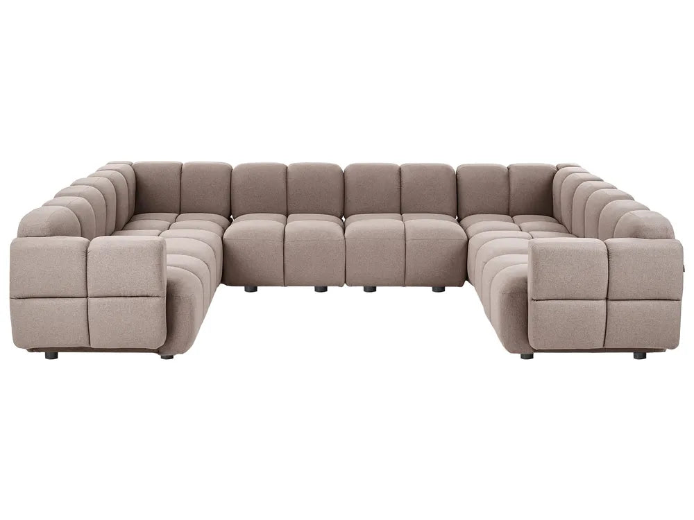 A modular sectional sofa upholstered in a textured taupe fabric, featuring a low-profile, blocky design with deep channel tufting on the arms and backrests, shown against a plain white background.