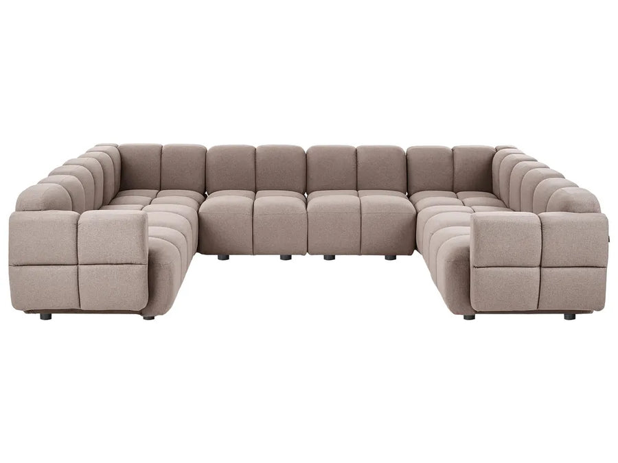 A modular sectional sofa upholstered in a textured taupe fabric, featuring a low-profile, blocky design with deep channel tufting on the arms and backrests, shown against a plain white background.