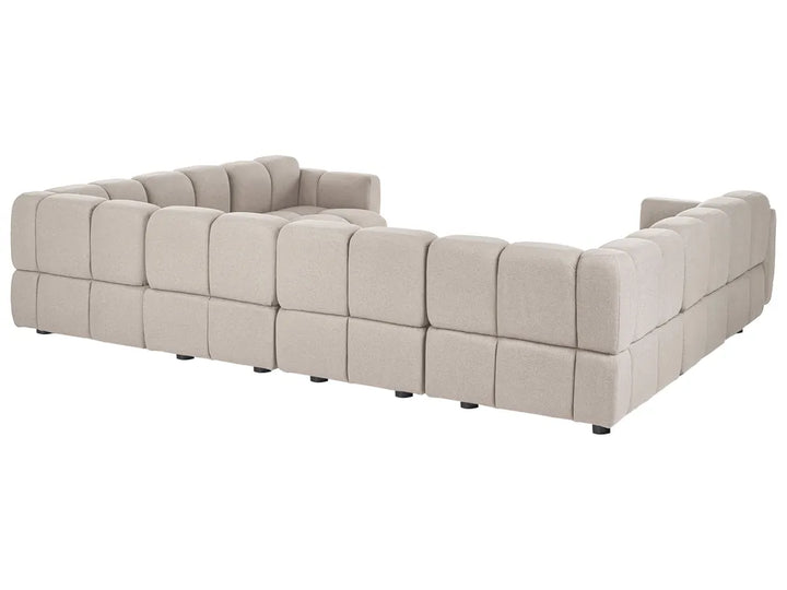 A modular tufted sectional sofa in a light beige fabric, shown from a three-quarters angle against a plain white background.