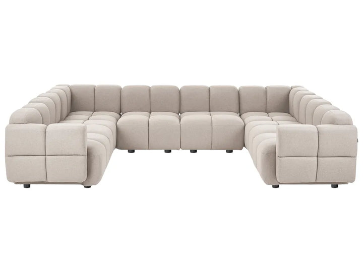 A modular sectional sofa upholstered in a light beige textured fabric, featuring a modern blocky design with deep channel tufting on the backrests and armrests, shown against a plain white background.