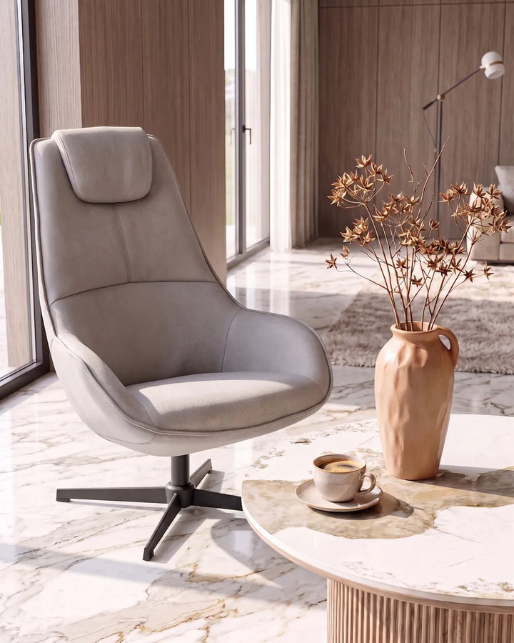 A modern high-back swivel lounge chair upholstered in light taupe fabric, set in a contemporary living room with a marble floor, a round marble-top coffee table, a ceramic vase with dried branches, and a cup of coffee.