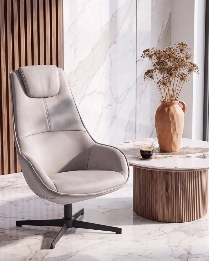 A modern light gray upholstered swivel lounge chair with a black star base, styled in a contemporary room next to a marble-top side table with a terracotta vase of dried flowers.