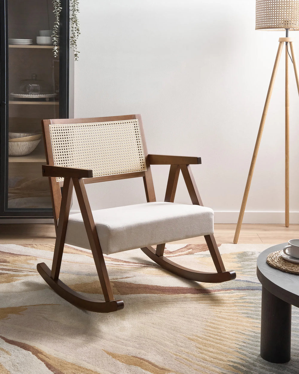 Wooden rocking chair with woven backrest in a room setting with a lamp and table.