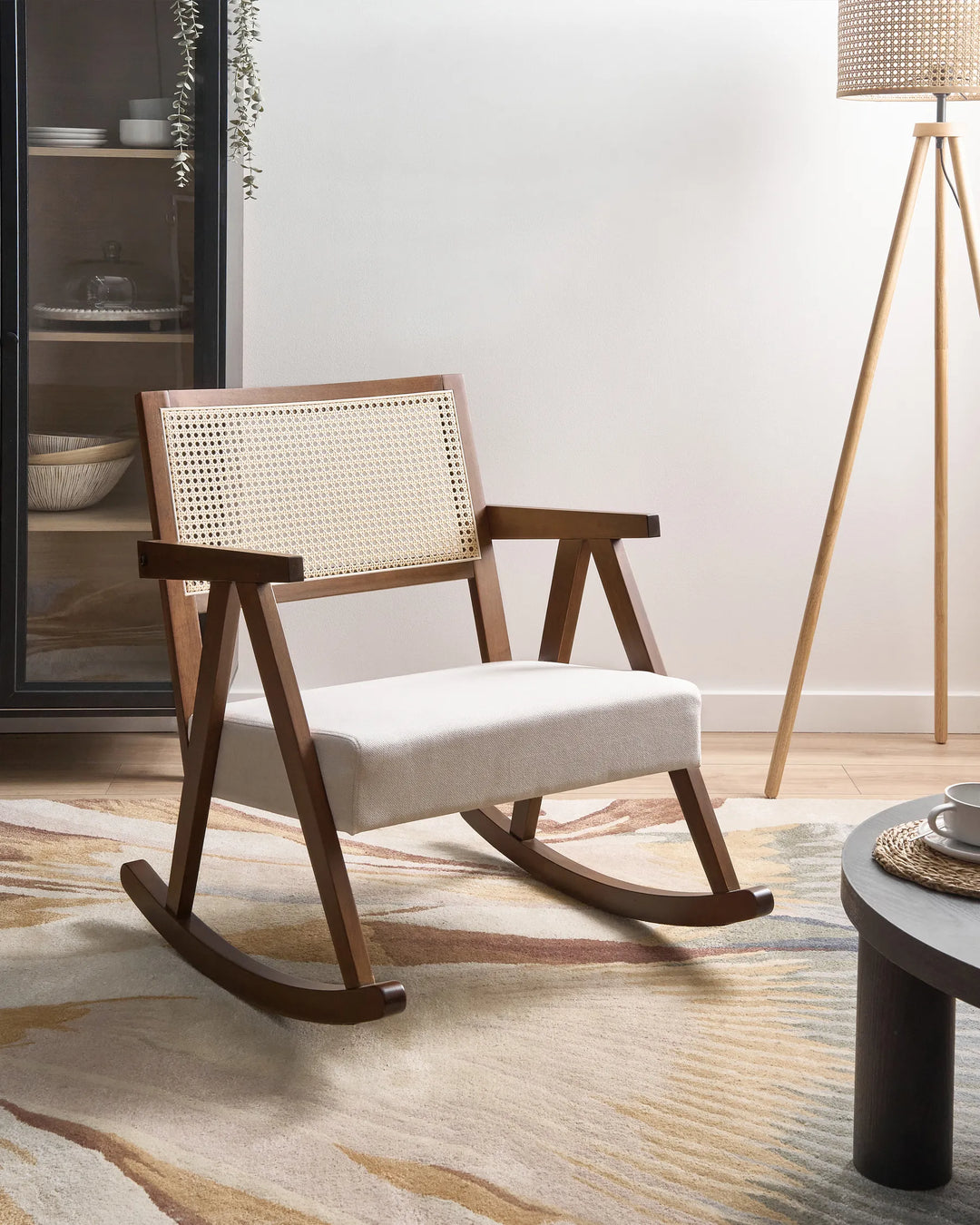 Wooden rocking chair with woven backrest in a room setting with a lamp and table.