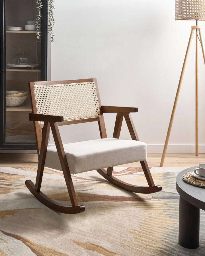 Wooden rocking chair with woven backrest in a room setting with a lamp and table.