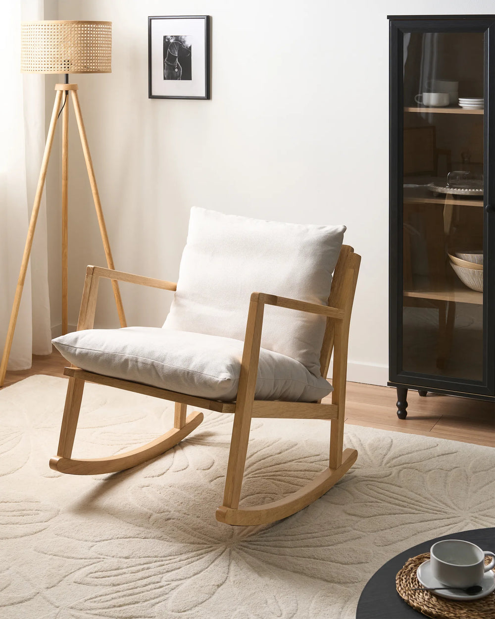 Wooden rocking chair with white cushion in a room with a lamp and cabinet.