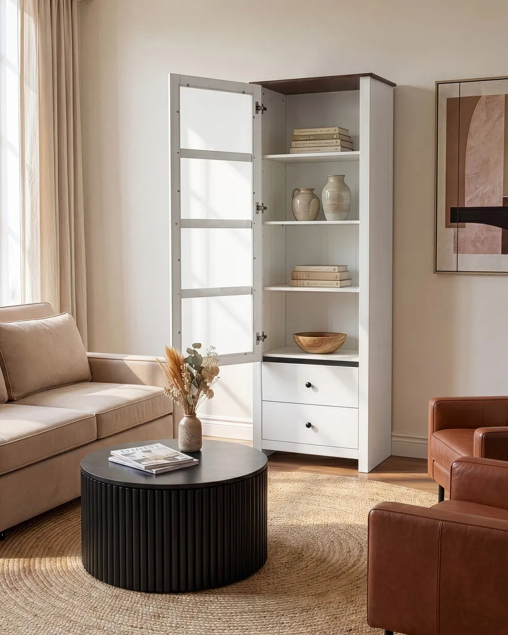 A tall white storage cabinet with glass-paneled doors and open shelves stands in a styled living room beside a beige sofa and round black coffee table.