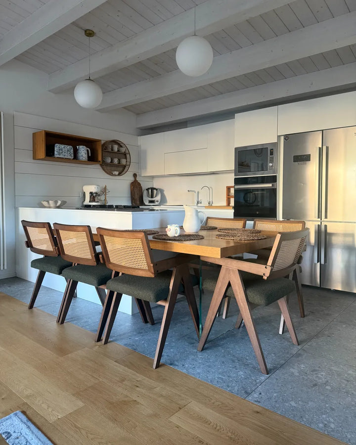 Modern kitchen with wooden dining table and chairs, stainless steel appliances, and white walls.