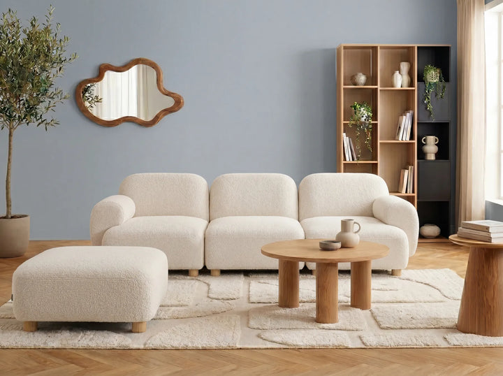 A modern three-seater sofa with a right-side chaise lounge, upholstered in a textured cream bouclé fabric and supported by light natural wood legs.