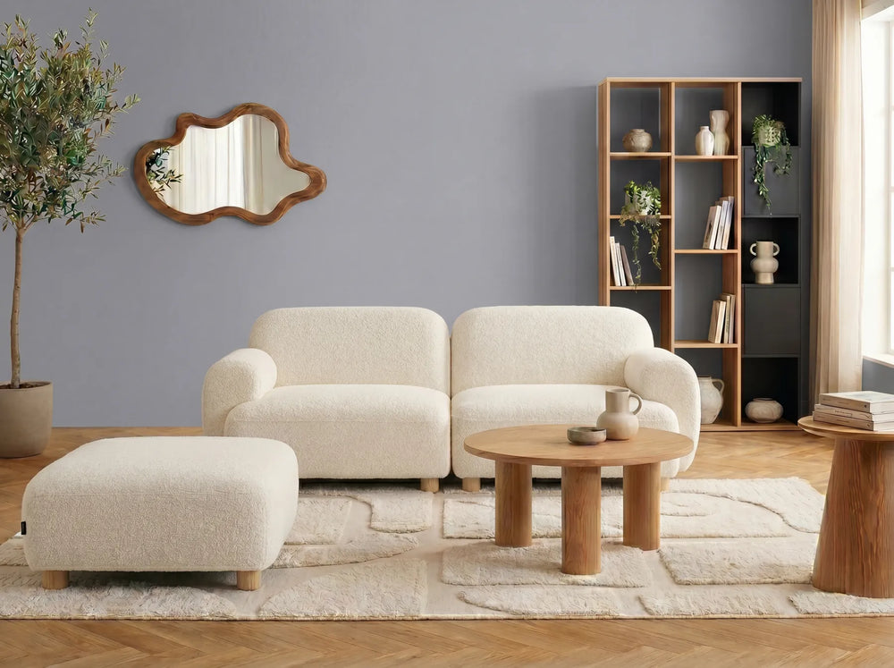 A modern two-seater sofa with a matching ottoman, upholstered in a textured boucle fabric in a light cream color, with small light wood legs.