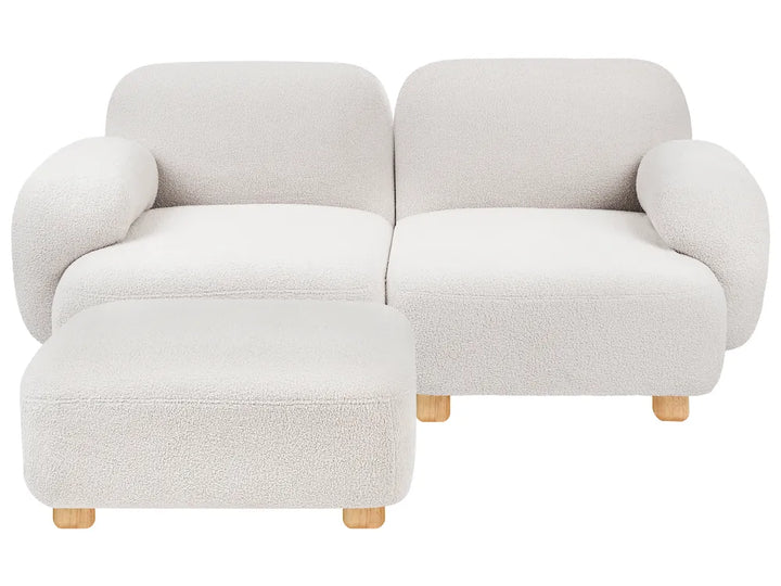 A modern two-seater sofa with a matching ottoman, upholstered in a textured boucle fabric in a light cream color, with small light wood legs.