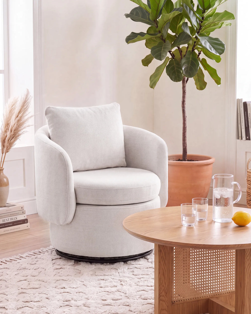 A light beige upholstered swivel armchair with a matching back cushion, placed in a bright, modern living room next to a wooden coffee table and a potted fiddle-leaf fig plant.