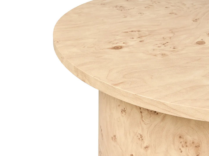 Close-up of a light natural wood table showing the round tabletop and matching cylindrical pedestal base on a white background.