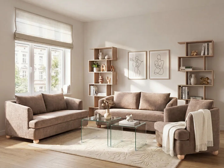 A styled living room featuring a coordinated furniture set including a taupe-brown fabric sofa, matching armchair, and a glass-top coffee table on a light rug, with open wooden shelving and framed wall art in the background.