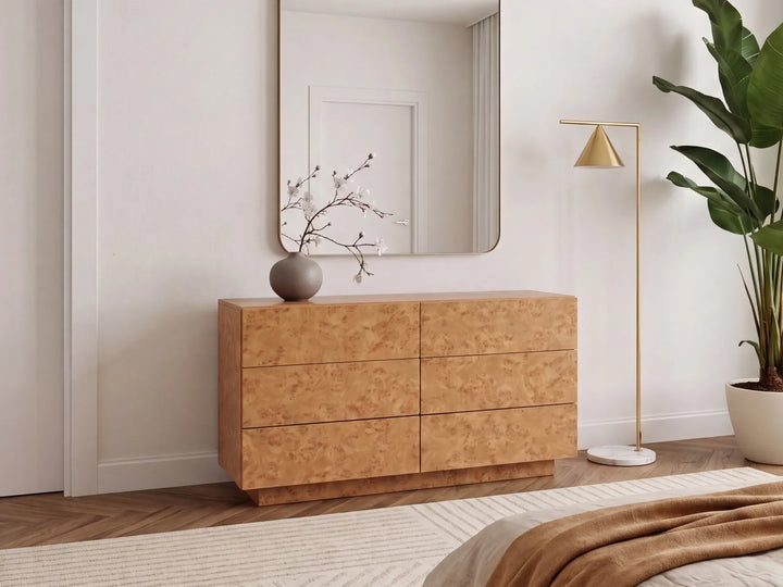 A modern six-drawer wooden dresser with a burl wood grain finish, styled in a minimalist bedroom setting with a matching wall mirror, a gold floor lamp, and a potted plant.