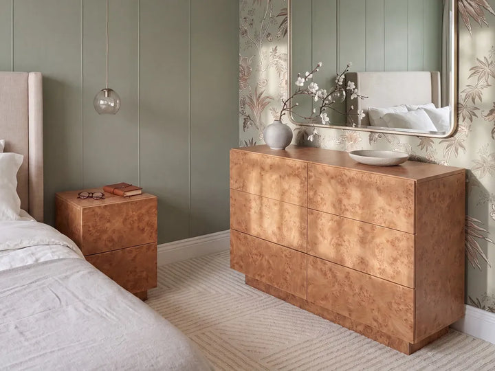 A modern bedroom featuring a large six-drawer chest of drawers in a distinctive swirling wood veneer finish, styled with a matching nightstand, a bed, and a mirror.