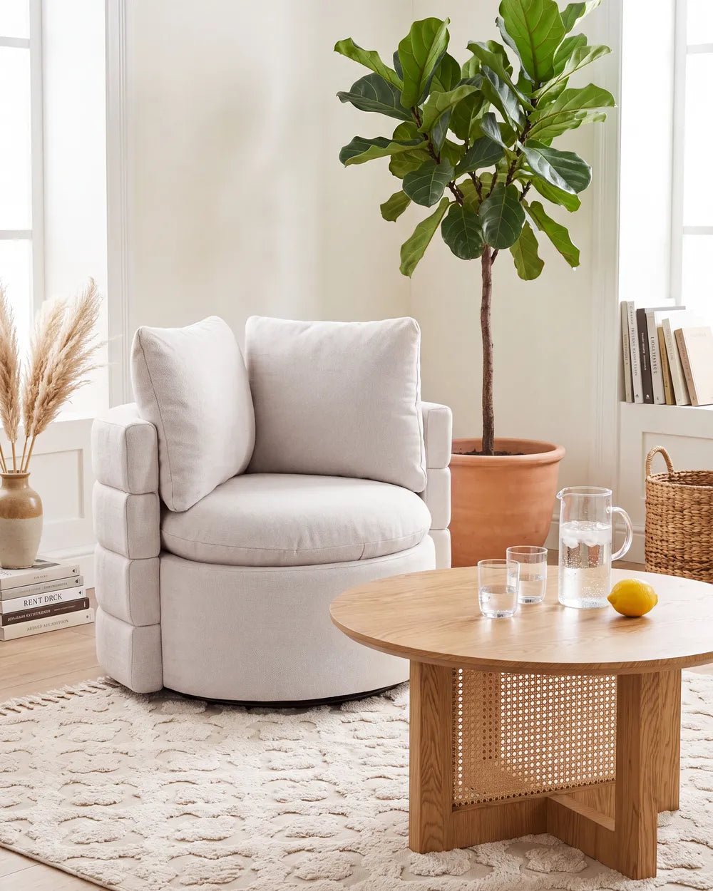 A light beige upholstered accent chair with two back cushions in a bright, modern living room setting next to a round wooden coffee table.
