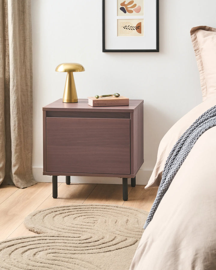 Wooden nightstand with a gold lamp and decorative items in a bedroom setting.