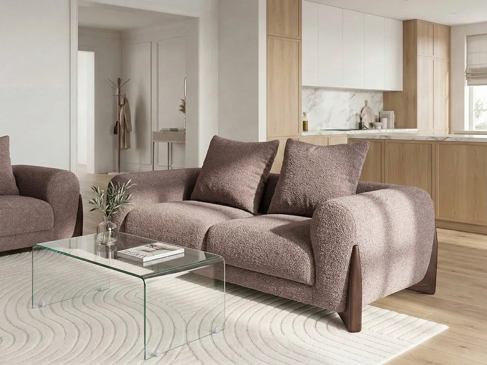 A modern textured fabric sofa in a warm taupe-brown color, styled in a contemporary living room with a matching armchair, a glass coffee table, and a patterned rug.