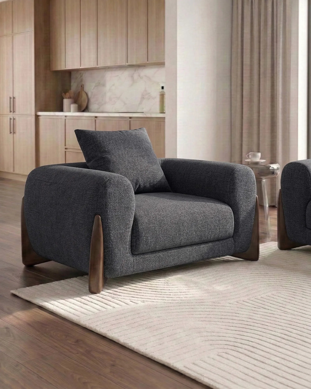 Gray armchair in a modern living room setting with wooden flooring and neutral decor.