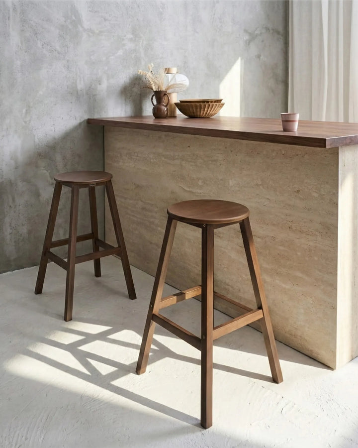 Two wooden stools in front of a wooden counter against a concrete wall.