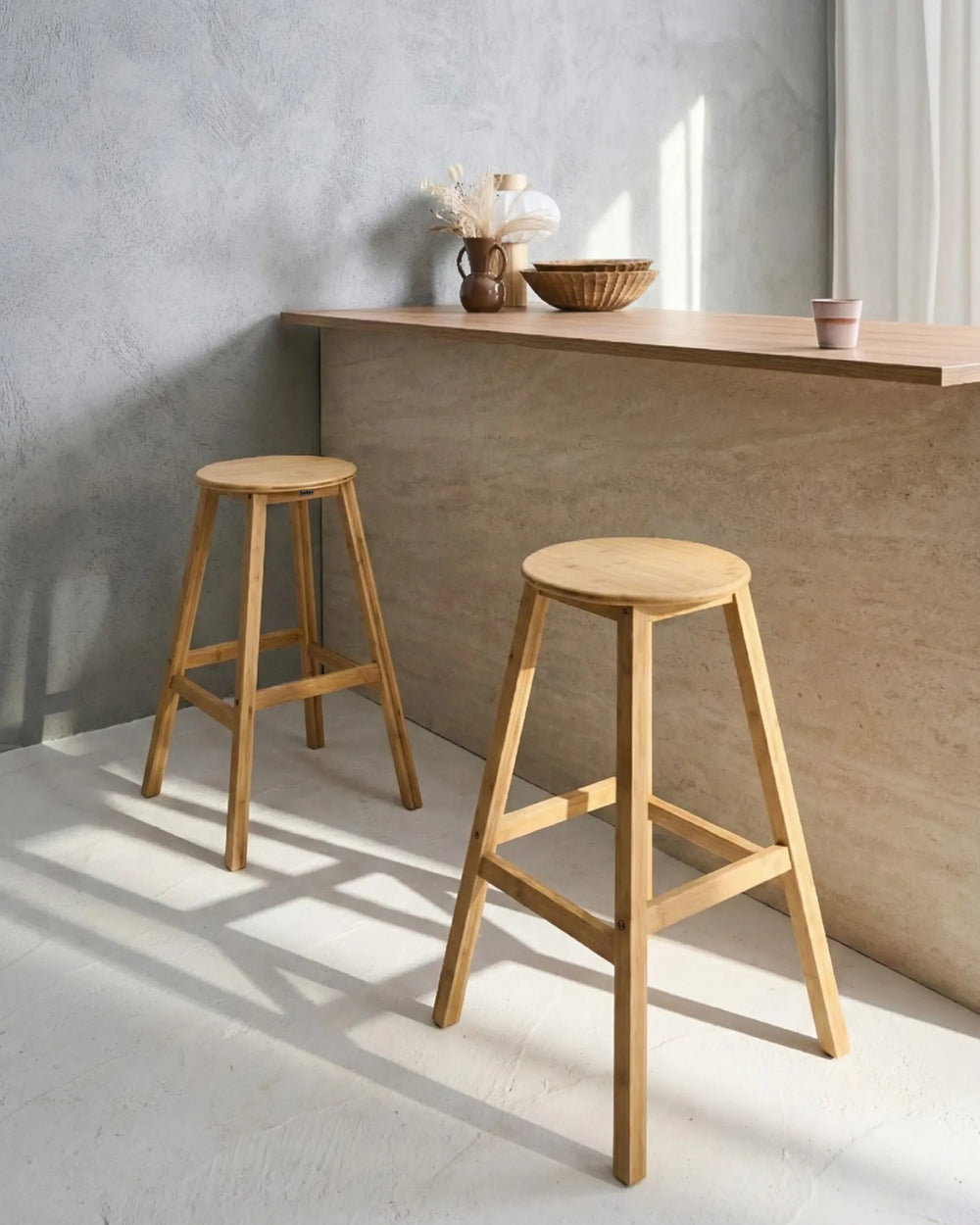 Two light natural wood A-frame bar stools in a minimalist room with a concrete wall and a wooden counter.