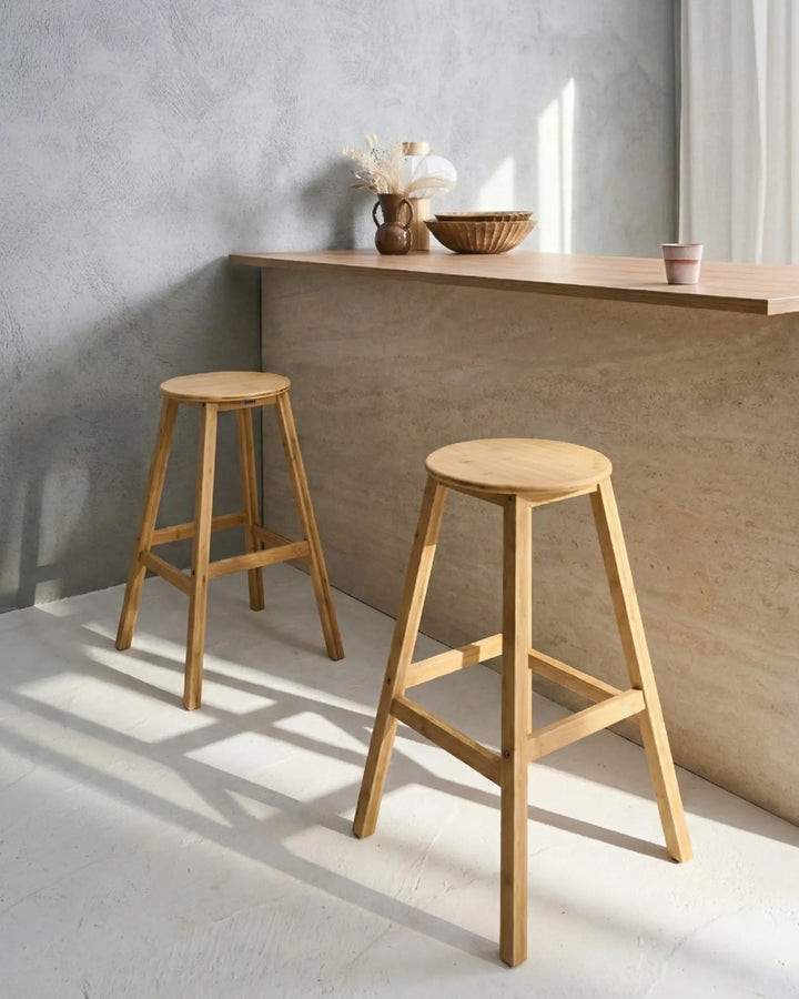 Two light natural wood A-frame bar stools in a minimalist room with a concrete wall and a wooden counter.
