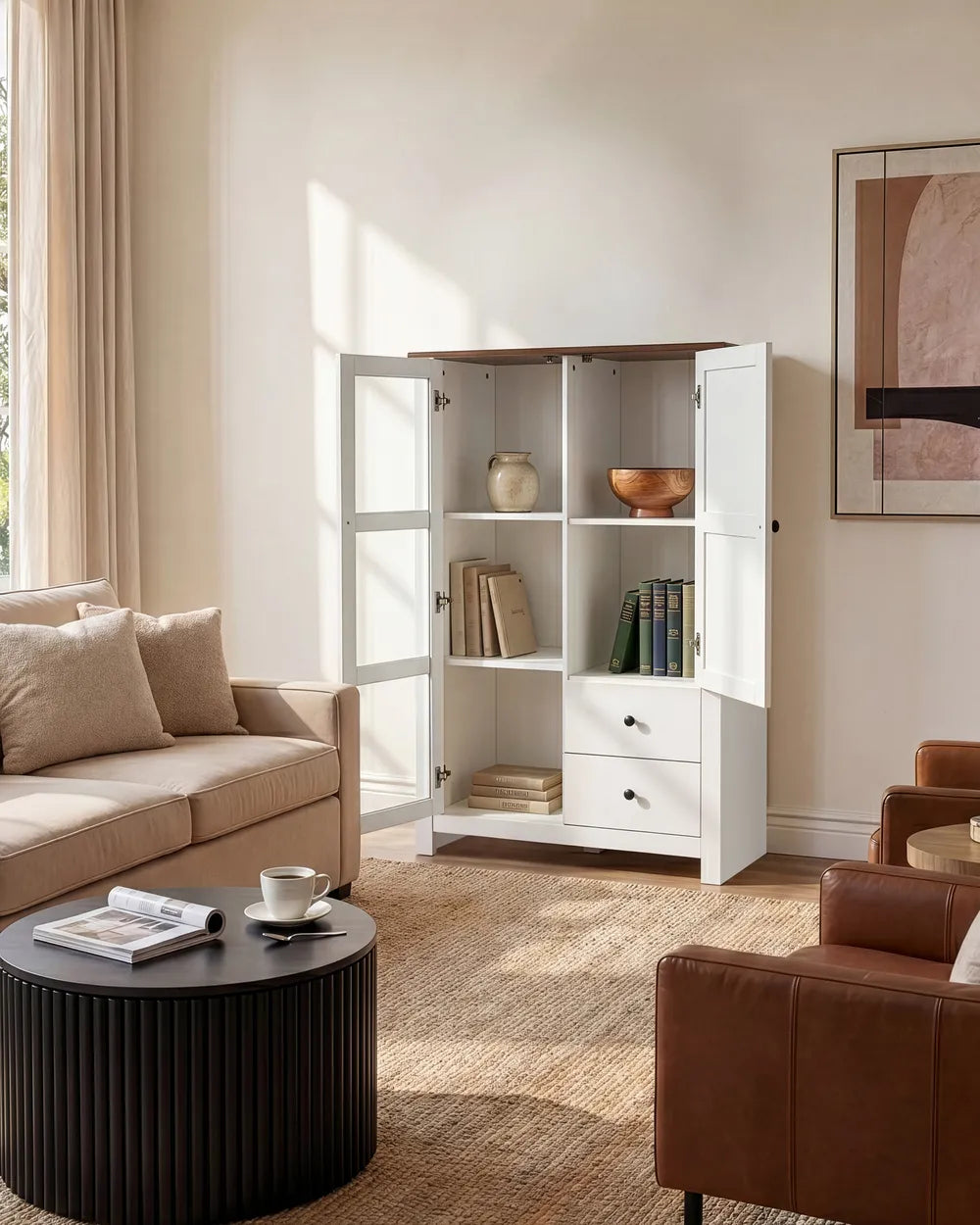 A white open bookcase cabinet with glass-paneled doors and three drawers, styled in a warm beige living room next to a sofa and coffee table.