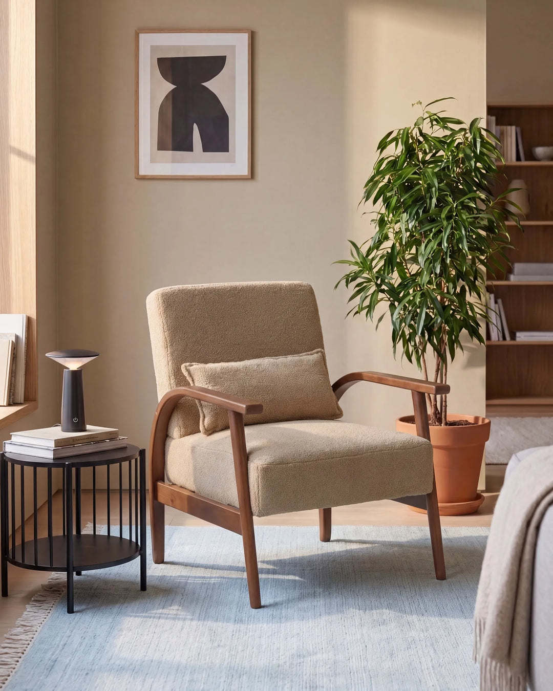 A mid-century modern armchair with beige textured upholstery and a wooden frame, styled in a warm, neutral-toned living room next to a black side table and a potted plant.