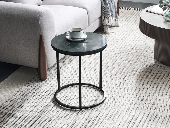Round side table with a black marble top and metal frame in a living room setting.