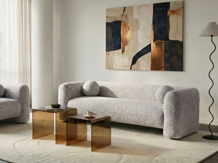 Modern living room with a gray sofa, abstract painting, and gold side tables.