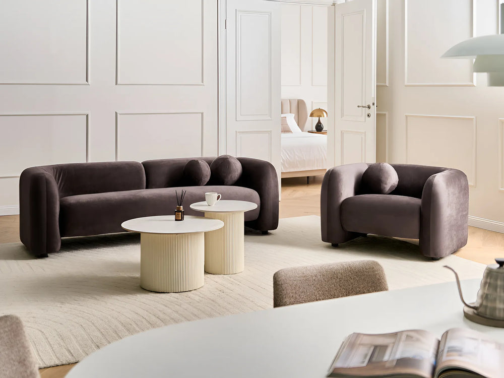 Modern living room with a purple sofa and armchair, white coffee table, and open book on a table.