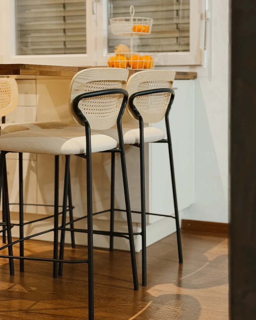 Three bar stools with black metal frames and white cushioned seats in a kitchen setting.