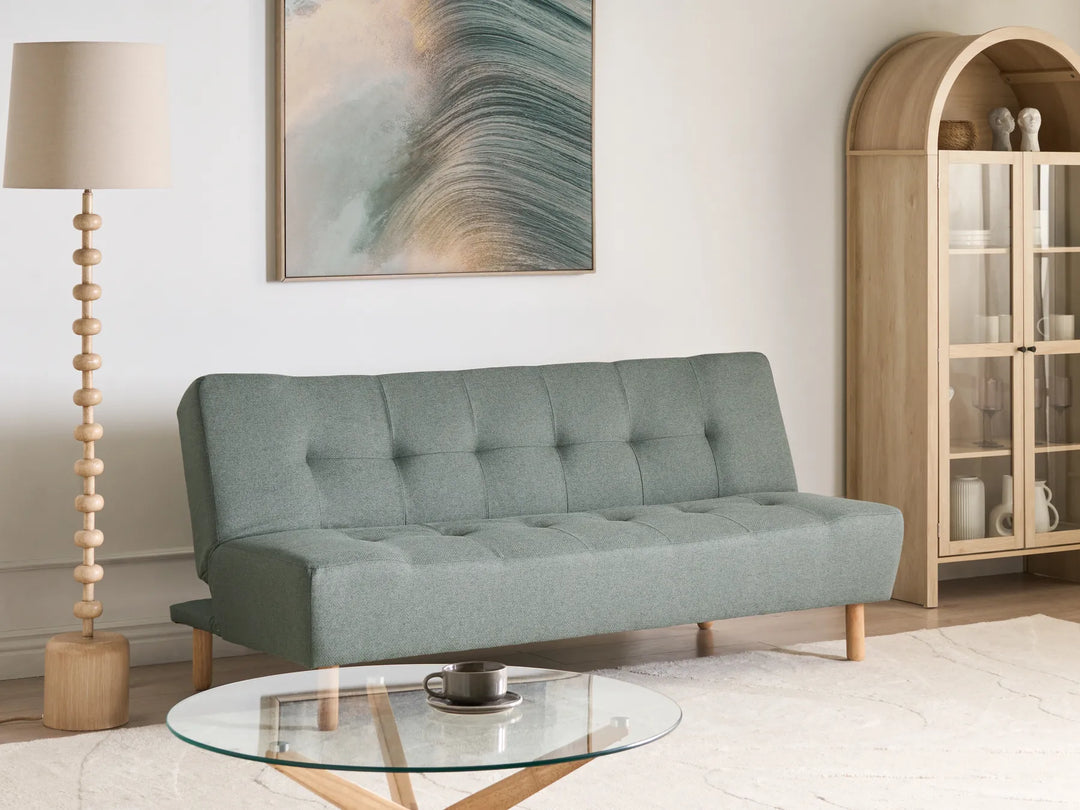 Gray sofa in a living room with a glass coffee table, lamp, and decorative items.