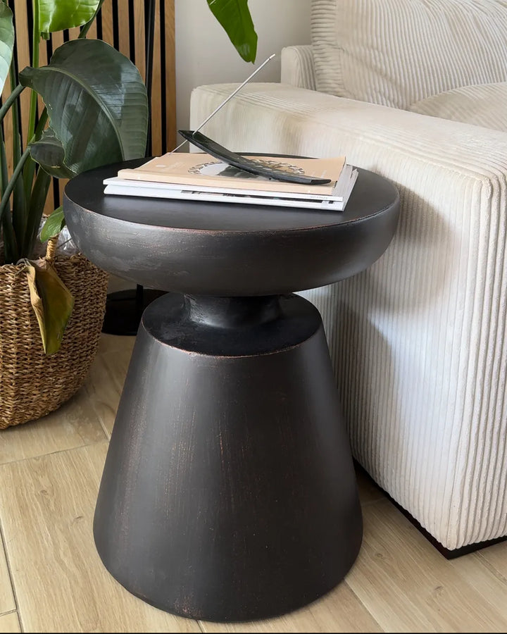 Black side table with a laptop and book next to a white armchair in a room.