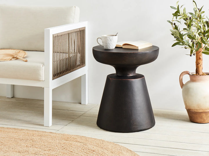 Dark wooden side table with a white mug and book in a minimalistic room.