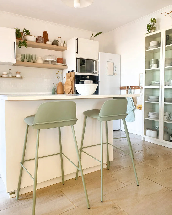 Modern kitchen with green bar stools, white countertops, and a refrigerator.