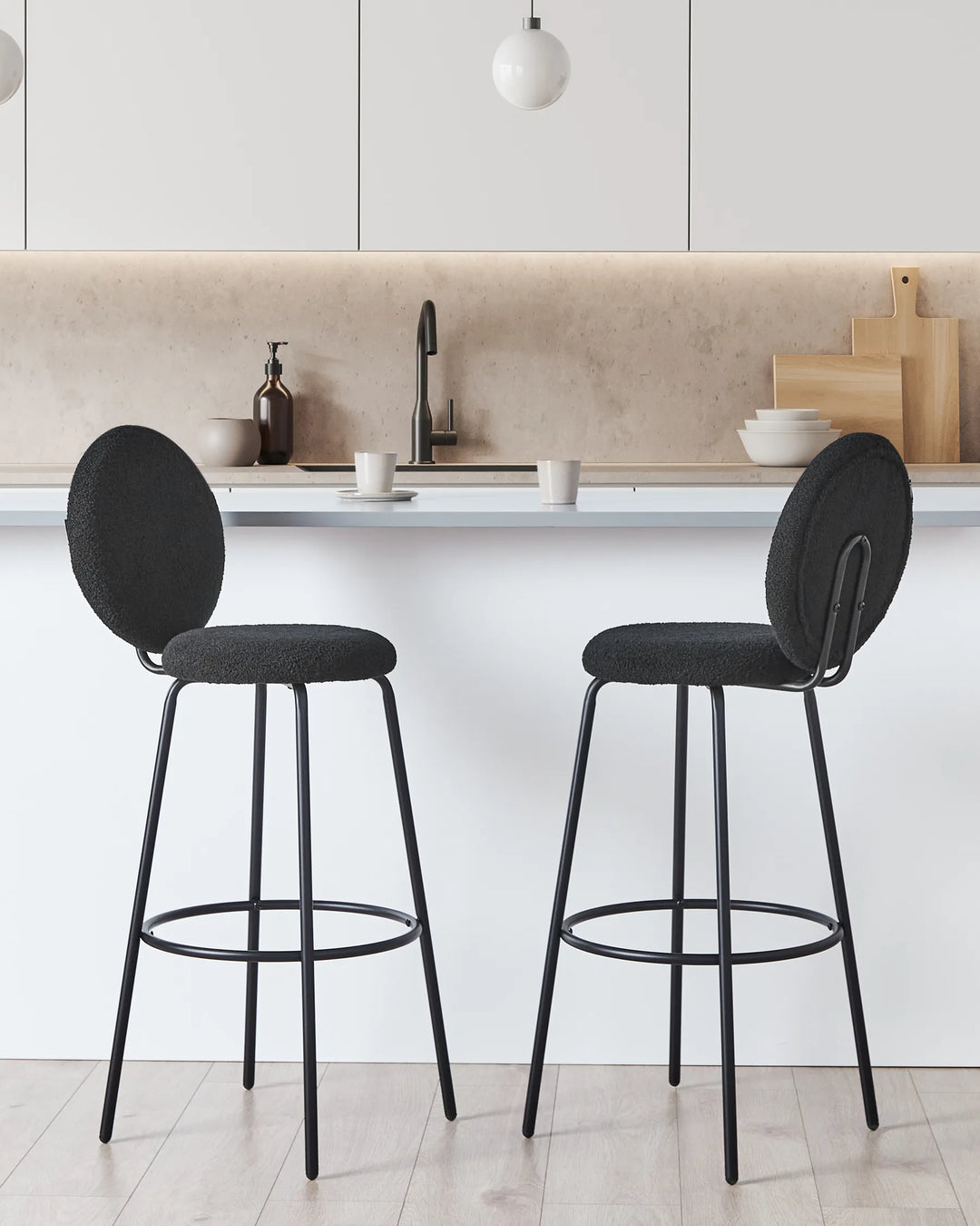 Two modern black bar stools with oval upholstered seats and backs, shown in a bright minimalist kitchen setting.