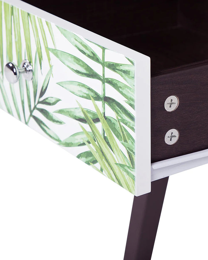 Close-up of a drawer front with a green palm leaf print on a white background, shown open to reveal a dark wood interior and silver knobs.