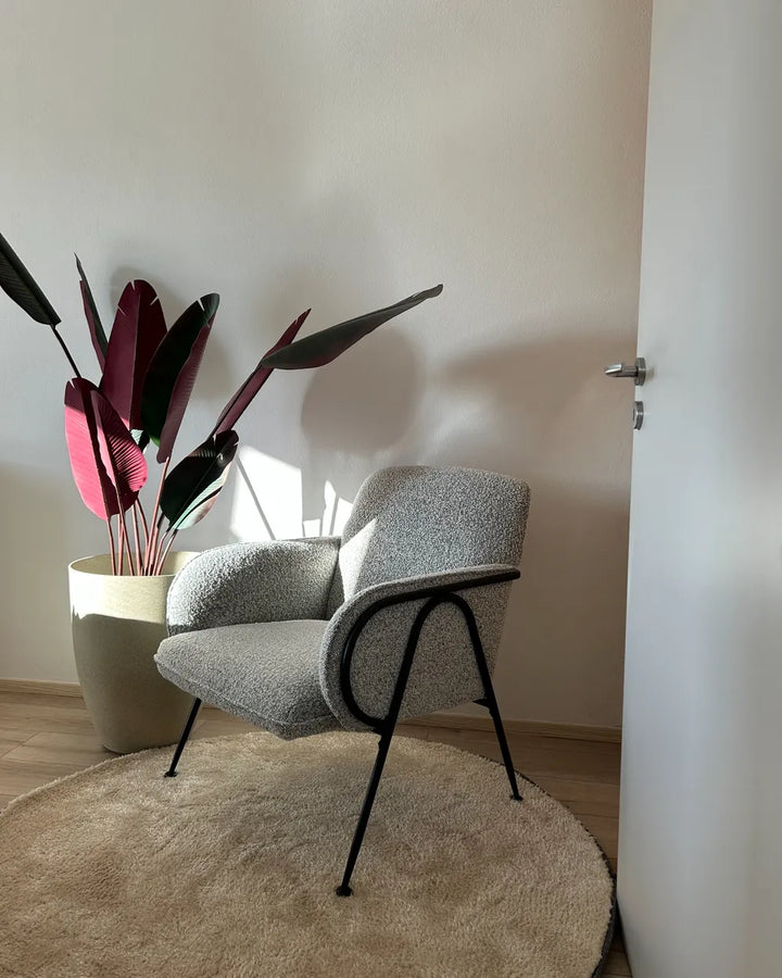 Gray armchair with black legs in a room with a plant and white wall.
