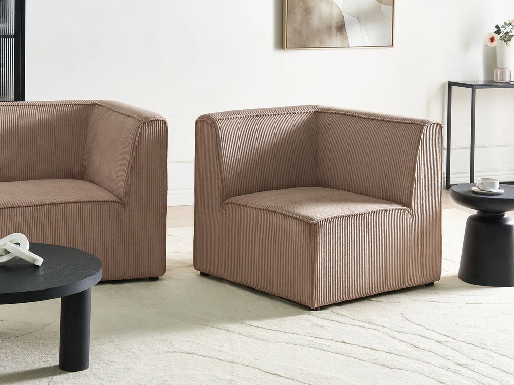 A modern two-seater armchair upholstered in a textured taupe corduroy fabric, shown in a minimalist living room setting alongside a matching armchair, black coffee tables, and a light-colored rug.